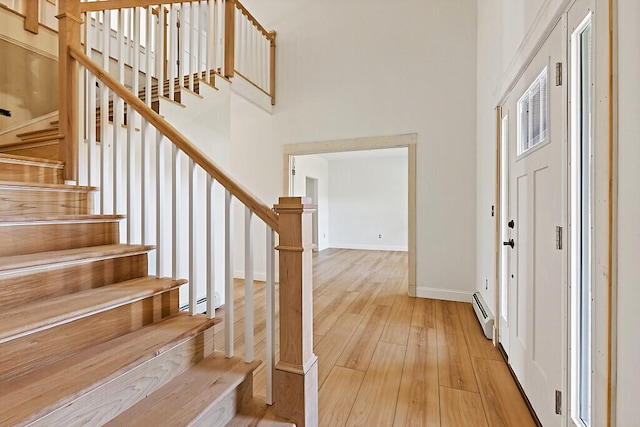 foyer with a baseboard heating unit, light wood-type flooring, and a high ceiling