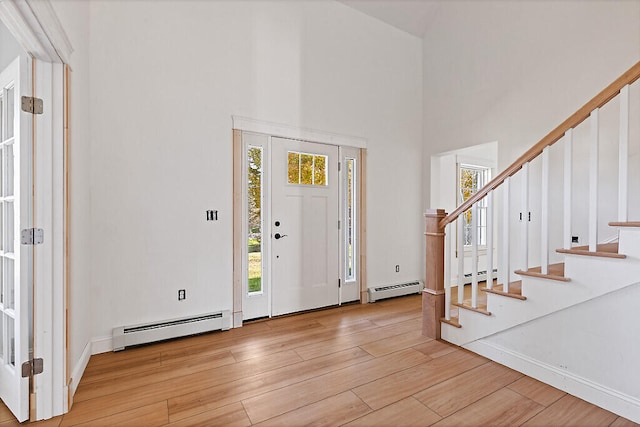 foyer entrance featuring a towering ceiling, light hardwood / wood-style flooring, and baseboard heating