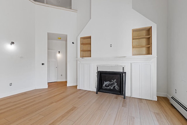 unfurnished living room featuring light hardwood / wood-style flooring, baseboard heating, a high ceiling, and built in shelves