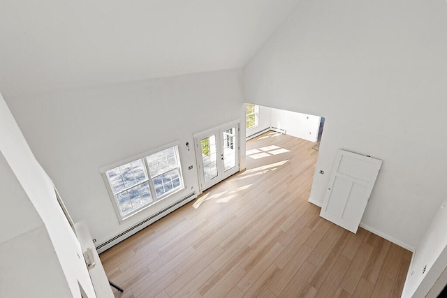 unfurnished living room featuring a wealth of natural light, light hardwood / wood-style floors, a baseboard heating unit, and high vaulted ceiling