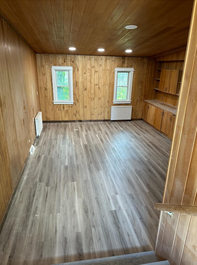 unfurnished room with light hardwood / wood-style flooring, wooden walls, and radiator