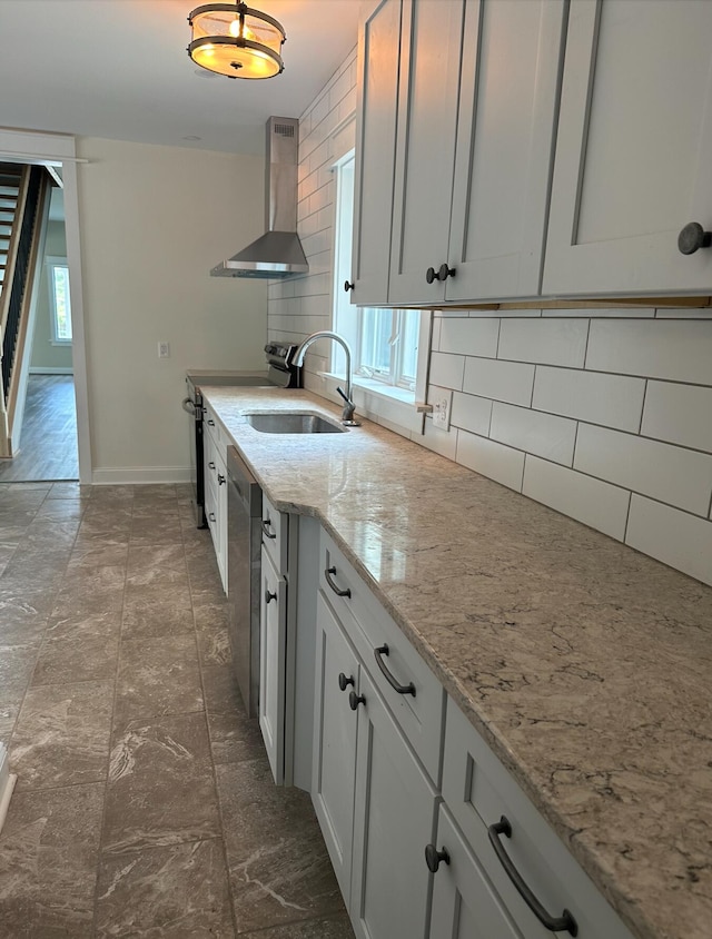 kitchen featuring backsplash, a healthy amount of sunlight, light stone counters, and wall chimney range hood