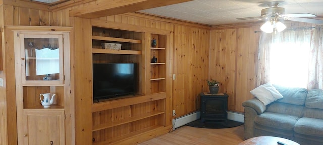 living room with a baseboard radiator, ceiling fan, wood walls, and a wood stove