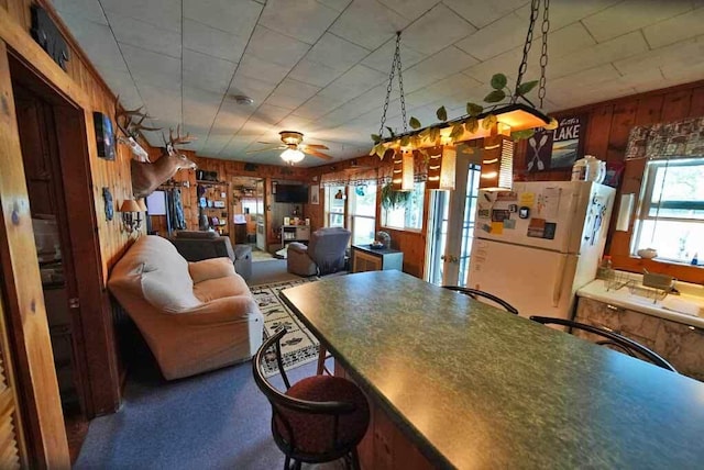 interior space with ceiling fan, wood walls, dark carpet, and plenty of natural light