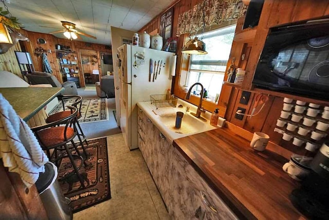 interior space with white refrigerator, wooden walls, ceiling fan, and sink