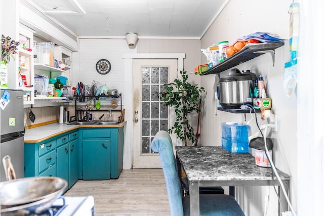 kitchen featuring light hardwood / wood-style flooring, blue cabinetry, crown molding, sink, and wooden walls