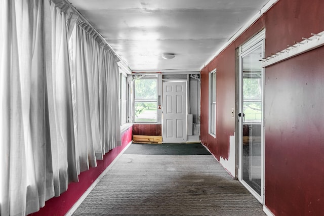 corridor featuring plenty of natural light and dark colored carpet