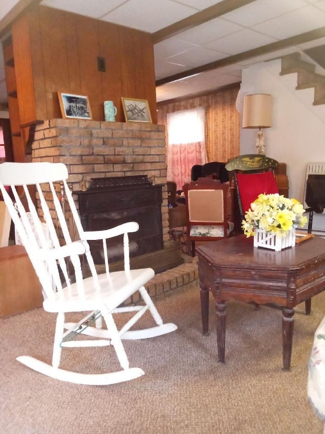 living room featuring a brick fireplace, wood walls, and dark carpet