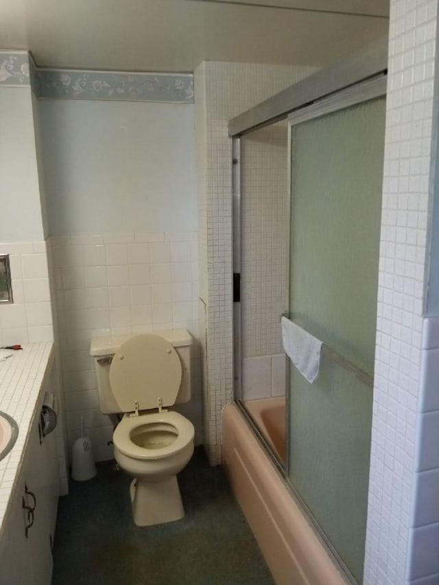 full bathroom with tile walls, toilet, vanity, tasteful backsplash, and bath / shower combo with glass door