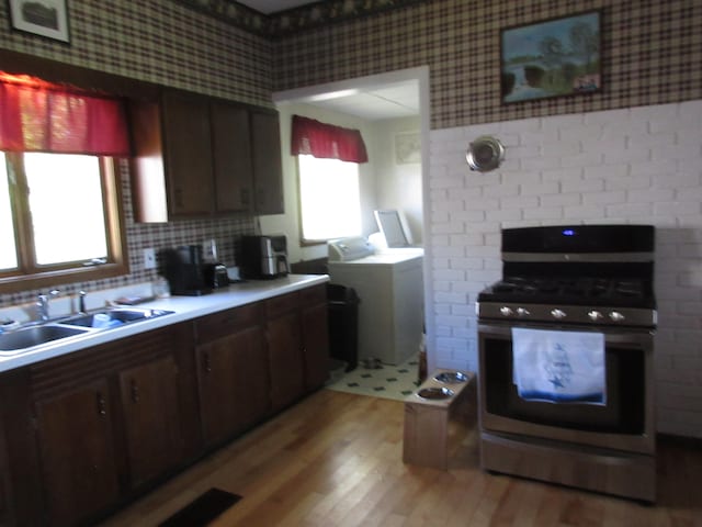 kitchen with stainless steel gas stove, dark brown cabinets, light hardwood / wood-style flooring, a fireplace, and sink