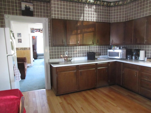 kitchen with dark brown cabinets, white refrigerator, tasteful backsplash, and light hardwood / wood-style floors