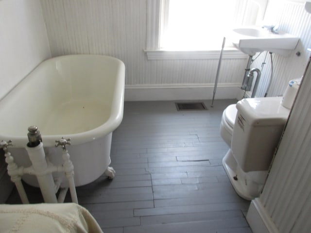 bathroom with a tub, toilet, and wood-type flooring