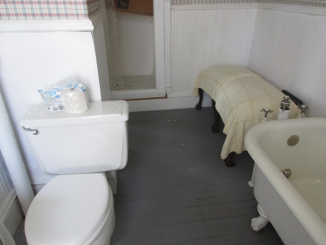 bathroom with toilet, a bath, and wood-type flooring