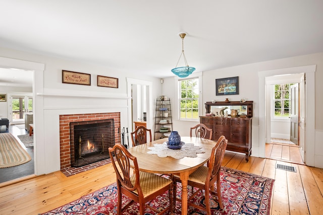 dining room featuring plenty of natural light, a brick fireplace, and light hardwood / wood-style floors