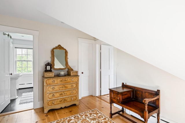 bedroom with baseboard heating, vaulted ceiling, and light wood-type flooring