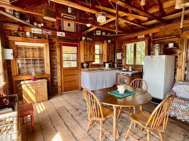 dining area with beam ceiling, light hardwood / wood-style floors, wooden walls, and sink