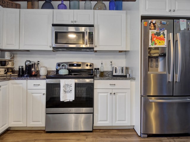 kitchen with stainless steel appliances, white cabinetry, and dark stone counters