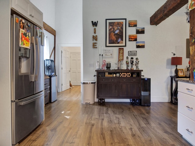 kitchen with stainless steel fridge, white cabinets, wood-type flooring, beamed ceiling, and dark brown cabinetry