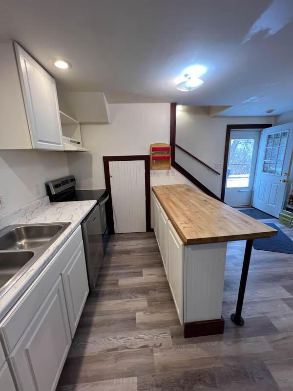 kitchen with sink, white cabinets, stainless steel electric range, wood-type flooring, and wooden counters