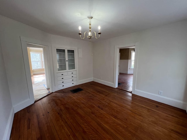 unfurnished dining area featuring a healthy amount of sunlight, dark hardwood / wood-style flooring, and a chandelier