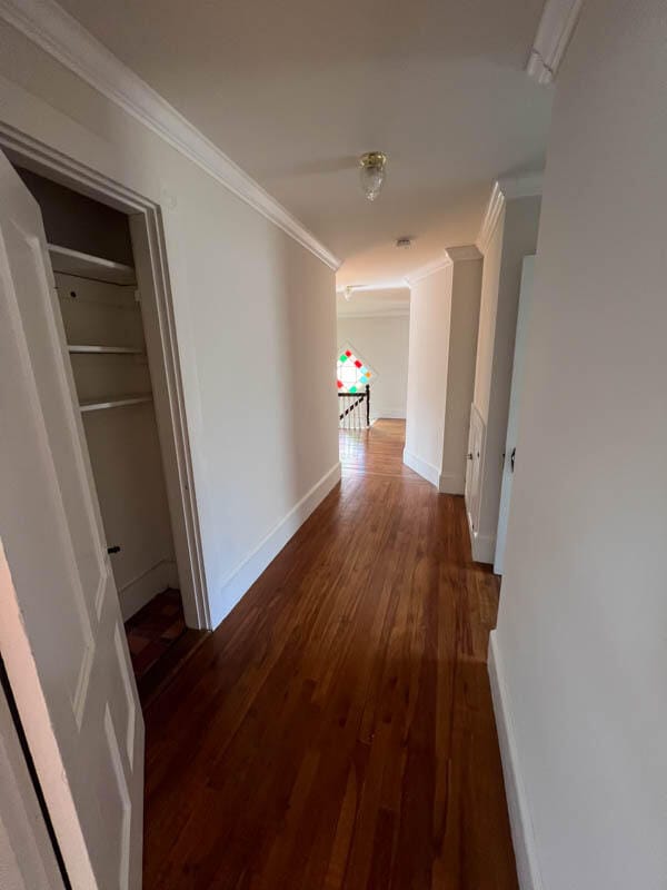 corridor with dark wood-type flooring and crown molding