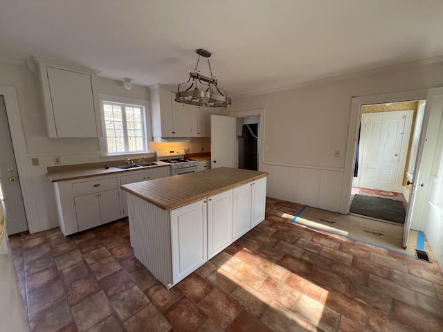 kitchen with decorative light fixtures, white gas stove, a kitchen island, white cabinets, and sink