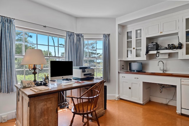 home office with plenty of natural light, built in desk, and sink