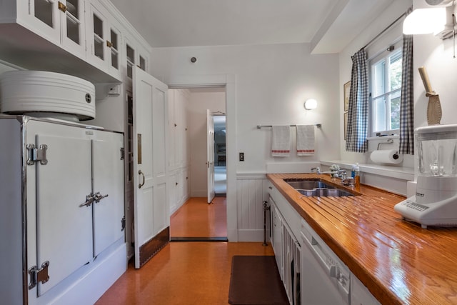 kitchen with stainless steel dishwasher, butcher block counters, sink, white cabinetry, and light hardwood / wood-style flooring