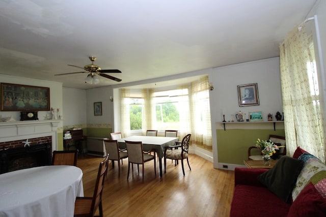 dining space featuring wood-type flooring, ceiling fan, and a brick fireplace