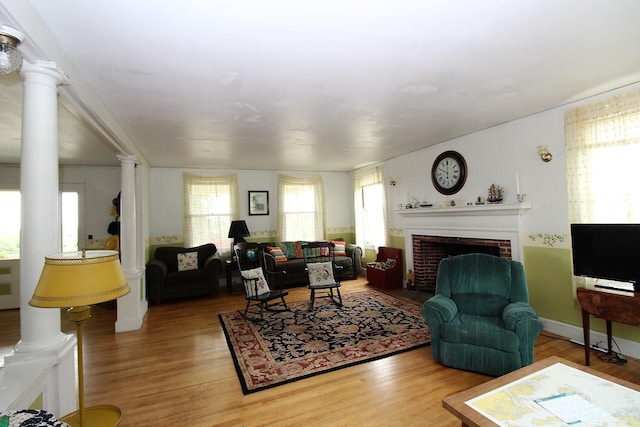 living room with a brick fireplace, light hardwood / wood-style floors, and ornate columns