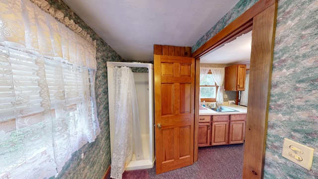 kitchen featuring carpet floors, brown cabinets, light countertops, a sink, and wallpapered walls