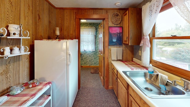 kitchen with white refrigerator, wood walls, dark colored carpet, and sink