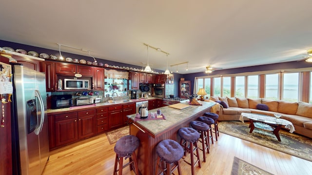 kitchen with decorative light fixtures, a kitchen bar, stainless steel appliances, ceiling fan, and light wood-type flooring