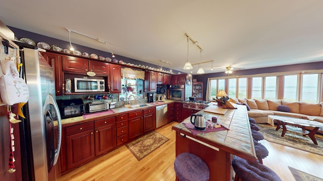 kitchen with light wood-type flooring, track lighting, sink, appliances with stainless steel finishes, and a breakfast bar area