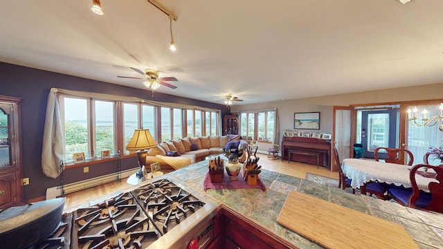 living area with ceiling fan with notable chandelier, a baseboard radiator, baseboards, and wood finished floors