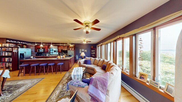 living room with light wood-type flooring, ceiling fan, a baseboard radiator, and indoor bar