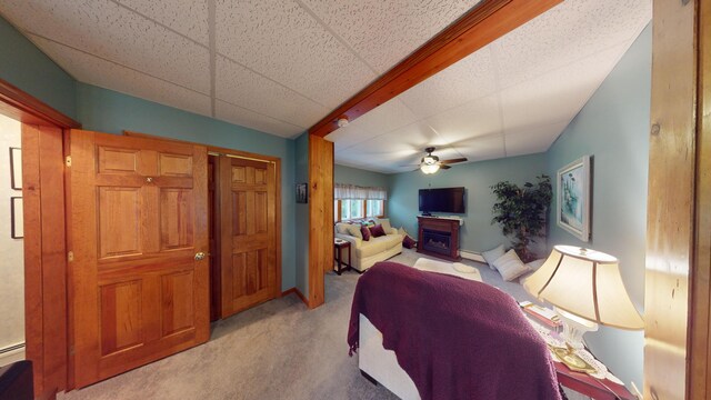 bedroom featuring a baseboard heating unit, ceiling fan, a drop ceiling, and light carpet