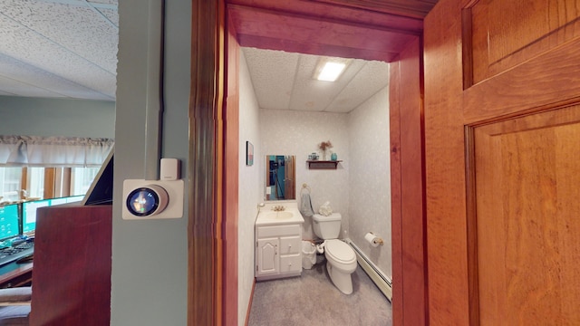 half bathroom with a baseboard radiator, a paneled ceiling, vanity, and toilet