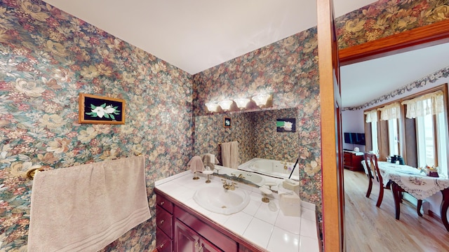 full bath with wood finished floors, a garden tub, vanity, and wallpapered walls