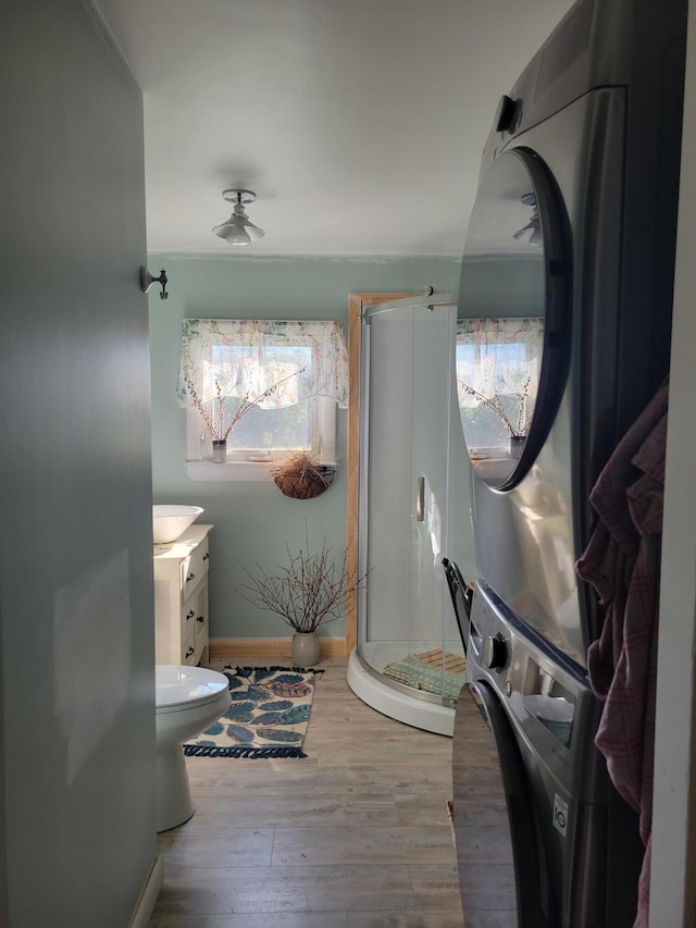 bathroom with toilet, vanity, a shower with door, wood-type flooring, and stacked washing maching and dryer