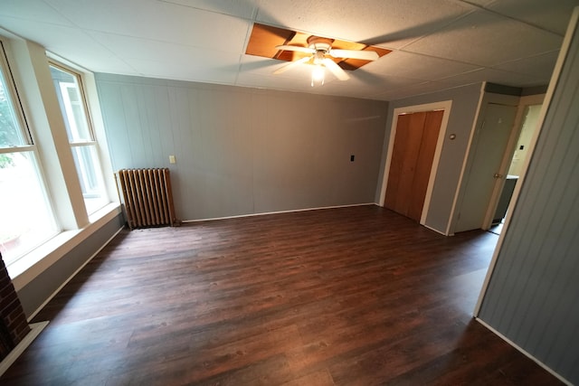 unfurnished room featuring ceiling fan, a drop ceiling, dark wood-type flooring, and radiator