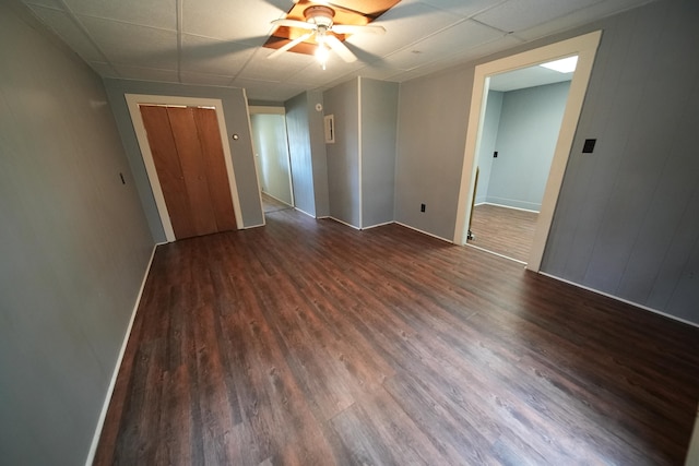 unfurnished bedroom featuring ceiling fan, a drop ceiling, and dark hardwood / wood-style flooring