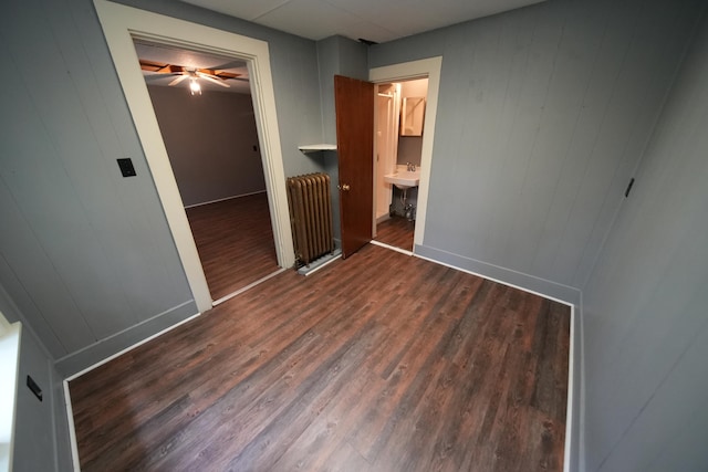 unfurnished bedroom with radiator heating unit, a closet, dark wood-type flooring, and sink