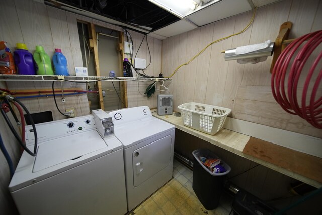 laundry area featuring light tile flooring, wooden walls, and washer and dryer