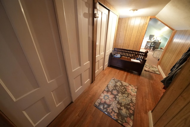 hallway with light hardwood / wood-style flooring, wood walls, and vaulted ceiling