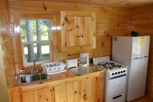 kitchen featuring white appliances, light brown cabinetry, wood walls, and sink