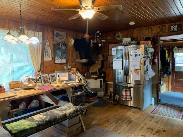 kitchen featuring ceiling fan with notable chandelier, wood walls, stainless steel refrigerator, and wood ceiling