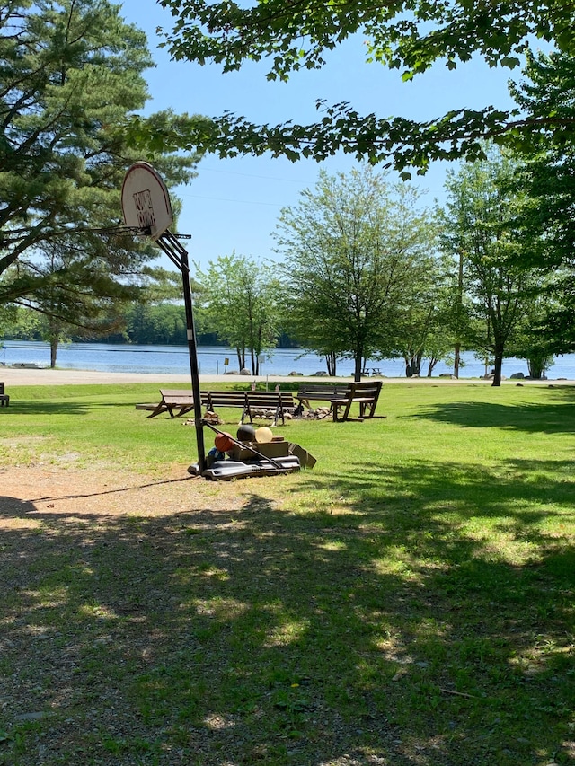 view of home's community with basketball hoop, a lawn, and a water view