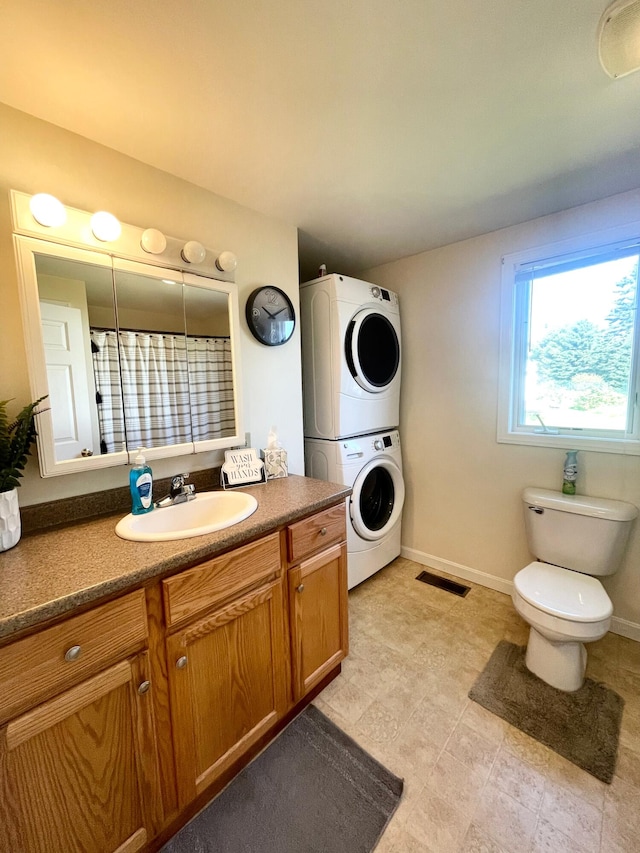 bathroom with tile floors, stacked washer / drying machine, toilet, and vanity