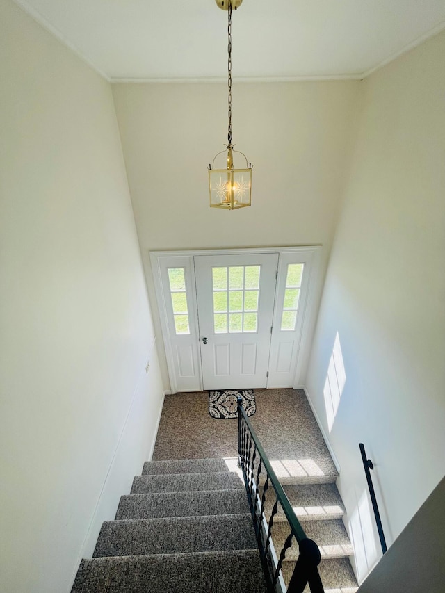 stairway with ornamental molding, a notable chandelier, dark carpet, and a high ceiling